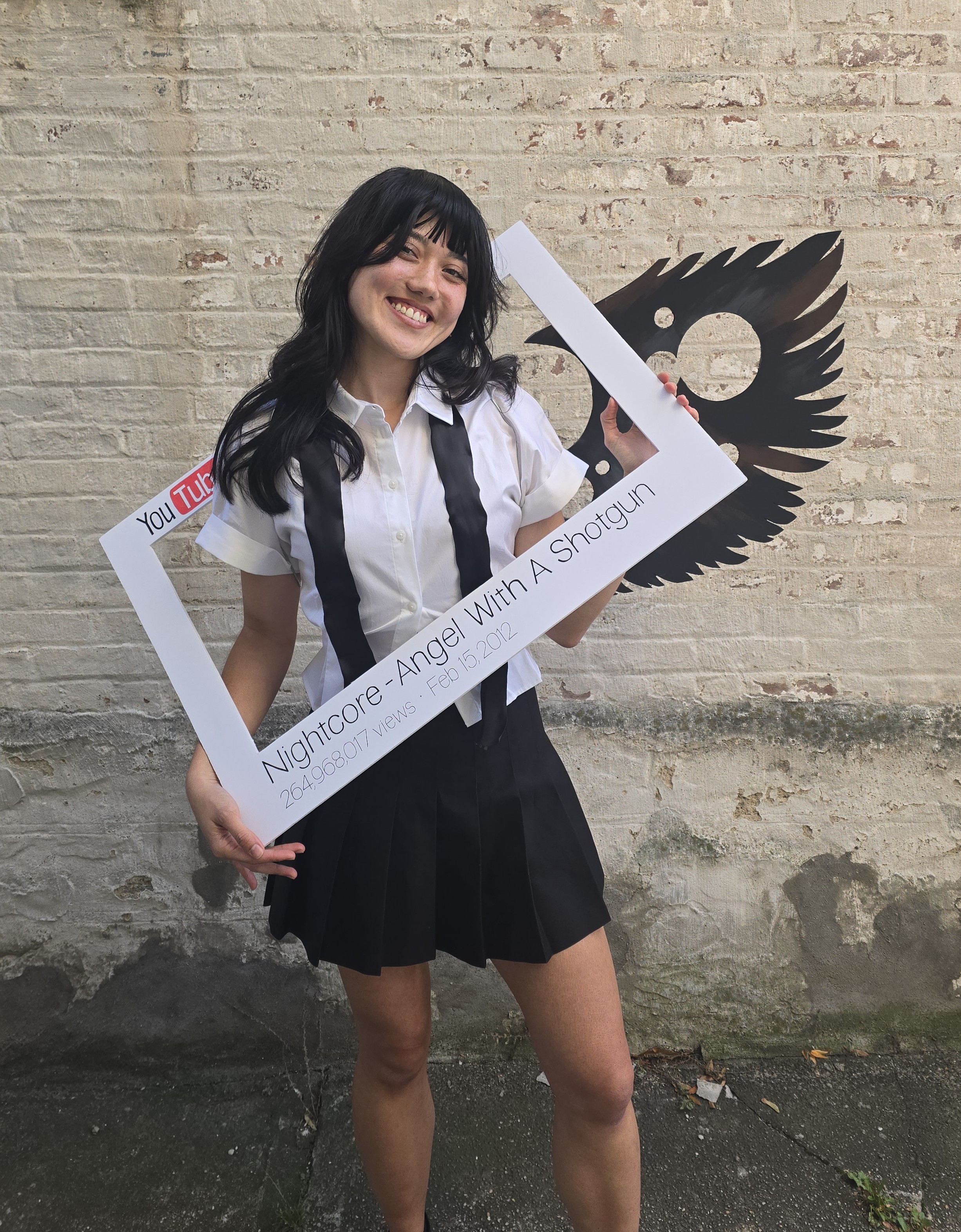 Heidi Erwin dressed as anime girl with black hair from the Angel With a Shotgun Nightcore video. Heidi holds a foam YouTube frame.