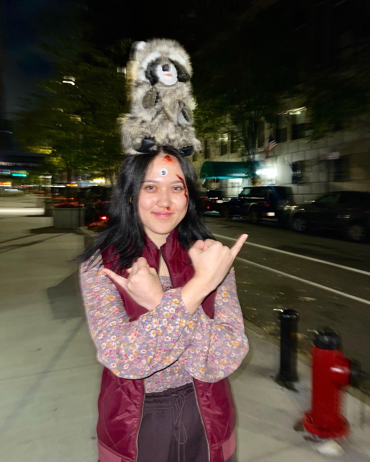 Heidi Erwin as Evelyn from Everything Everywhere All At Once outside on a Manhattan street at night with a raccoon puppet on her head.