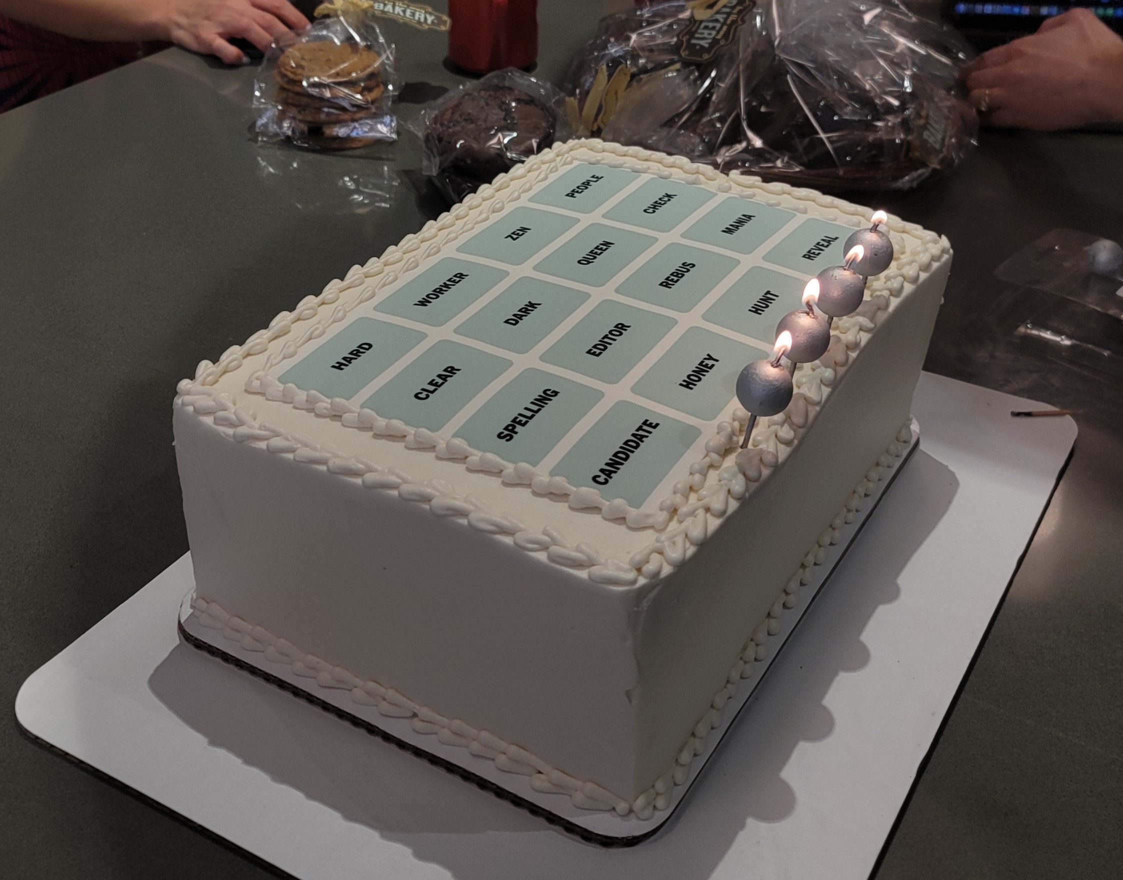 White rectangular cake featuring a Connections puzzle with the following words: HARD WORKER ZEN PEOPLE CLEAR DARK QUEEN CHECK SPELLING EDITOR REBUS MANIA CANDIDATE HONEY HUNT REVEAL.